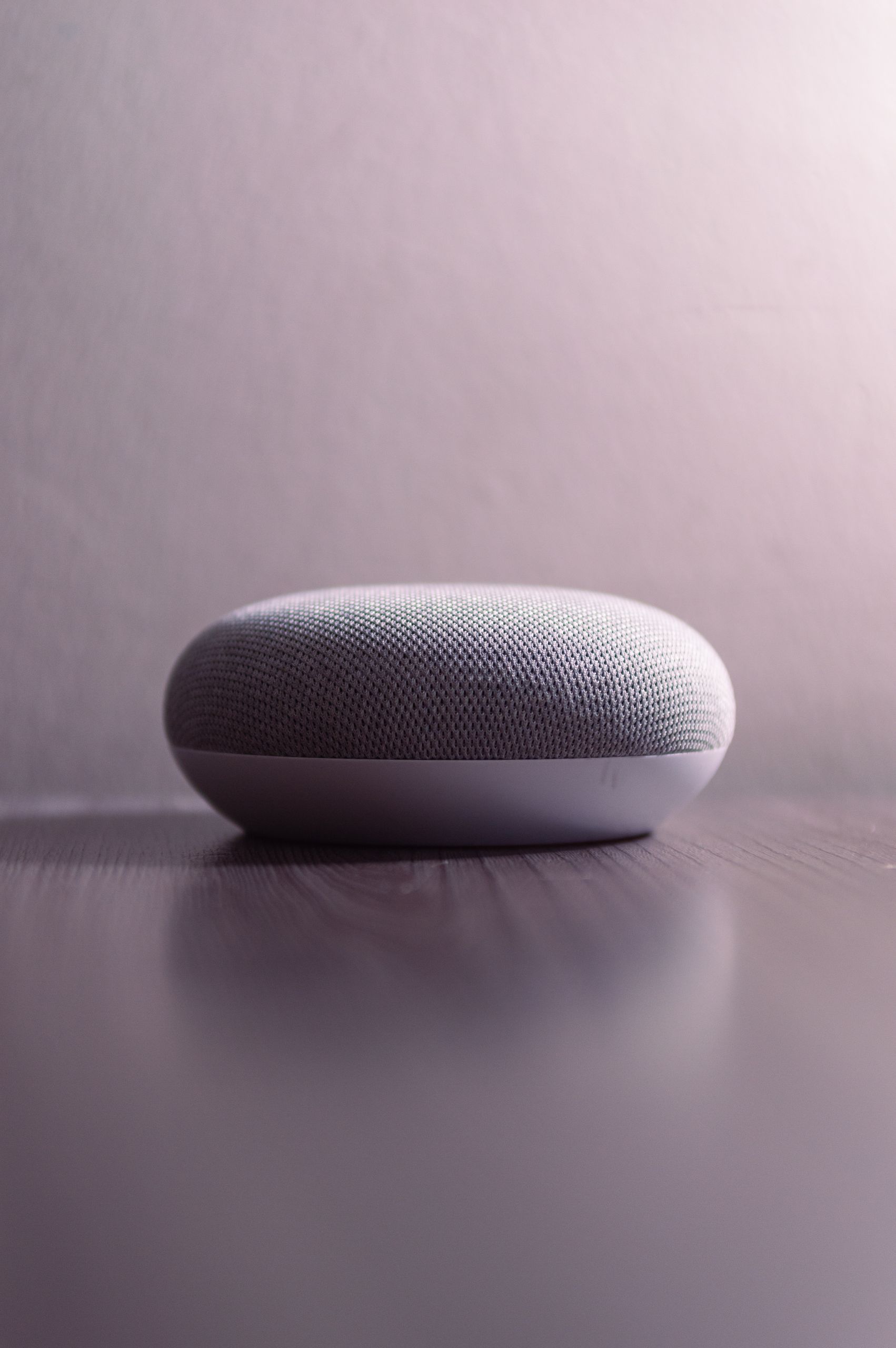 Close-up of a smart speaker on a wooden table with a soft light background.